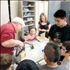 Ronan High School shop teacher Dave Edington does some drill work while his students help Sheila Hoback’s first graders make bird feeders last week.