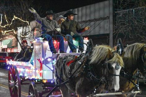 Drivers wave from atop a brightly lit horse-drawn holiday carriage.