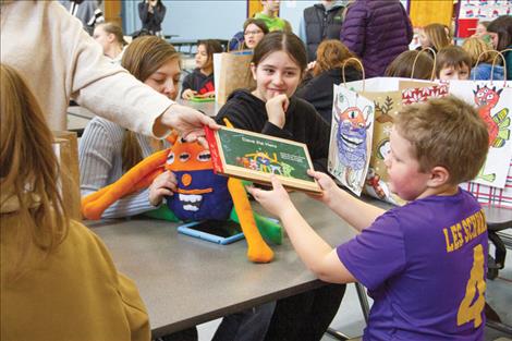 Jackson Mays is handed back his book “Dave the Hero,” the story of which was based on his drawing of a monster attached to a bag in the background.