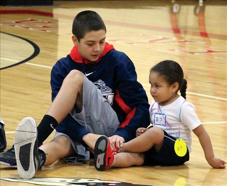 An itty bitty player learns the basics of stretching from an older helper.