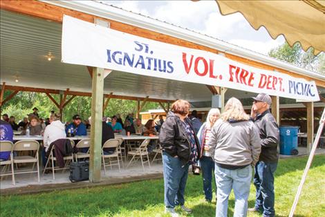 Community members stand outside of and sit under the Good Old Days Park pavilion during the live auction.