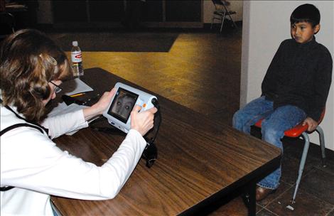 Polson Lions Club member Colleen Sperry uses a PlusOptix mobile vision screener to test student Stanley Redwood’s eyes.