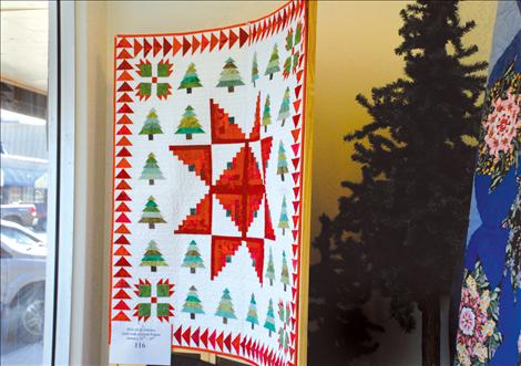 Christmas trees and log cabin blocks in greens and reds and a stack and whack quilt are two of the quilts in All In Stitches’ window.