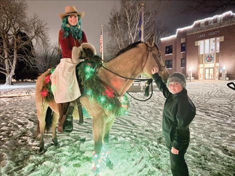 Lou and Tawni (her rescue horse), dressed up in festive colors, garland and lights for the annual tree lighting event to spread the message about their LES Haven blind horse rescue ranch. Rowan Goddard reaches up to pet Tawni after the tree is lit for the season.