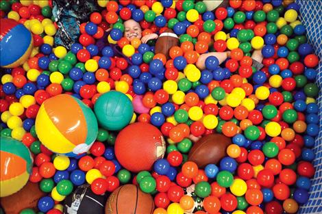 A small smiling face emerges from the ball pit.