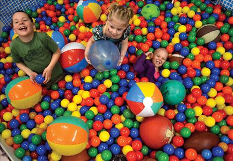 Three smiling faces emerge from the ball pit.