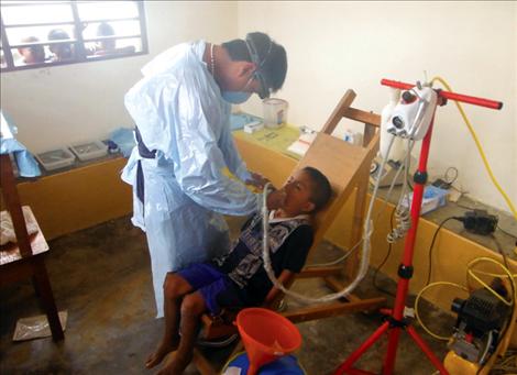 Carlos, the group’s dentist, drills a young boy’s tooth in the portable dentist’s chair. Other village children sneak a peek and wait their turn.