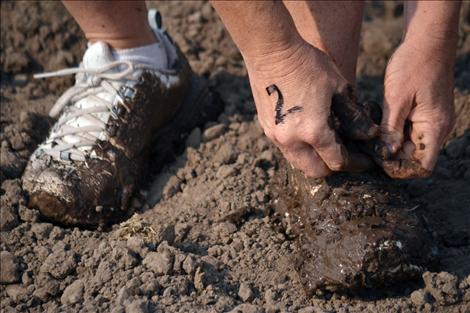 A participant stops to tie her shoelace through thick mud.