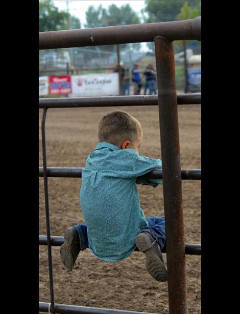 Wishing he was out there, a young cowboy watches from the sidelines at the fair.