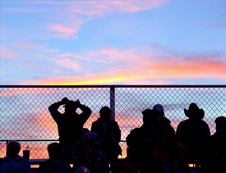 Fans watch a Ronan football game as the sun's departure leaves behind a palette of violet colors.