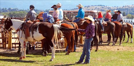 Waiting for the rodeo to start, high school athletes linger by the arena fence and one young man hangs onto his horse's tail. 