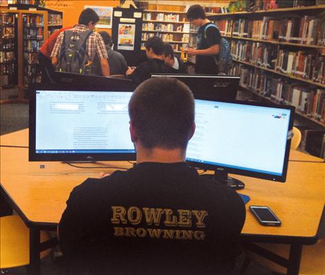 A Polson High School student works on a paper, utilizing double screens as other students work in the background.