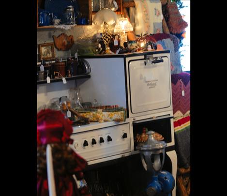 A vintage enamel stove, in  good condition, displays lots of vintage items, such as lamps, pie plates and crockery.