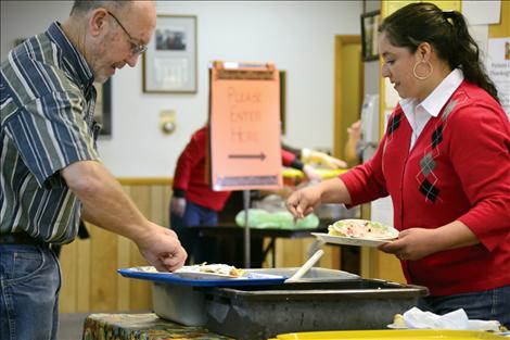 Volunteers C.W. Adams and Lupita Carillo clear plates, tossing paper dessert ones in the garbage and preparing the silverplate utensils and ceramic dinner plates to be washed.