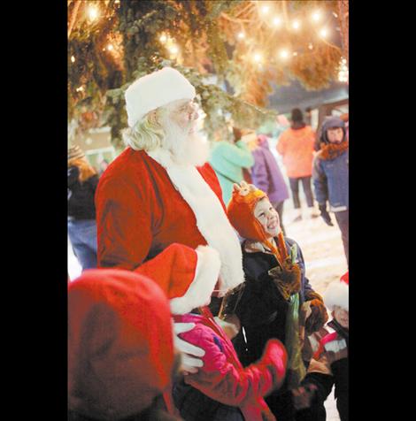 Santa Claus stands  in the middle  of a crowd of children beneath the town Christmas tree.