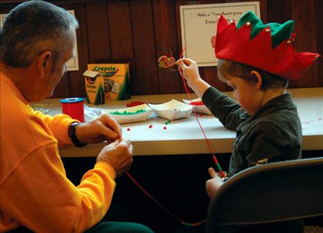 Aedan Dupuis strings a “Help the Grinch find a Heart” necklace with his grandpa Clay Herring. 