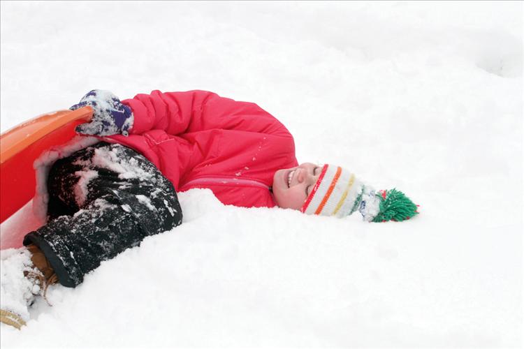 Following a snowy tumble,  a young sledder  giggles while enjoying a chilly rest on the wintery slopes of Polson Golf Course.