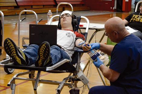 Laine Charlo, 18, double-tasks by working on his computer while he gives blood.