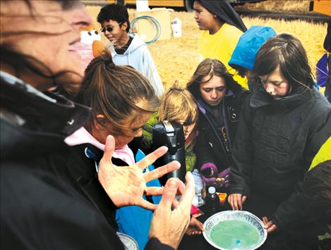 Rene Kittle, MSU Flathead extension agent, uses a bowl of milk to serve as an ecosytem and dish soap to illustrate invasive species as fourth-graders do an experiment about the effects of invaders on native plants and animals. 