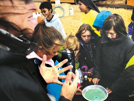 Rene Kittle, MSU Flathead extension agent, uses a bowl of milk to serve as an ecosytem and dish soap to illustrate invasive species as fourth-graders do an experiment about the effects of invaders on native plants and animals.