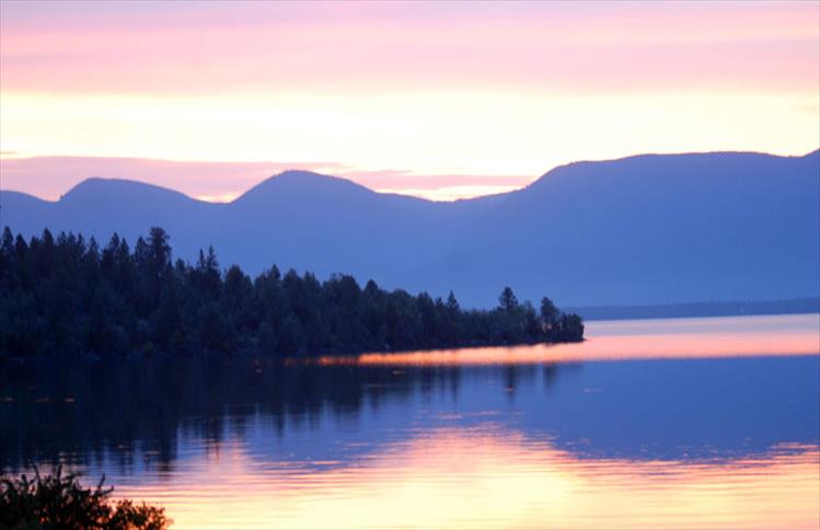 Sunrise paints Flathead Lake pink and orange as it peeks over the Mission Mountains.