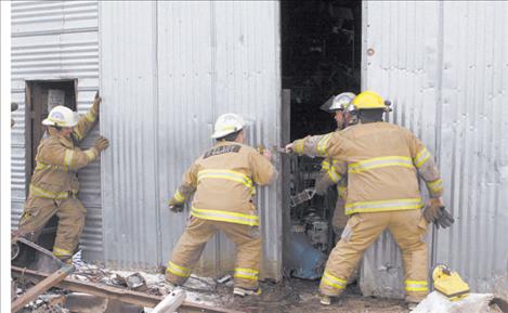 Ronan firefighters attempt to close sliding doors of the shop that caught on fire Monday afternoon. There were no injuries and minimal damage to the maintenance/junkyard shop belonging to Leroy Lake.
