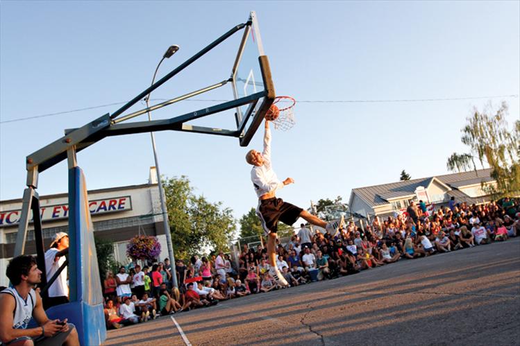 Spectators line the  sidewalks as an athlete dunks the ball while warming up for the slam dunk contest.