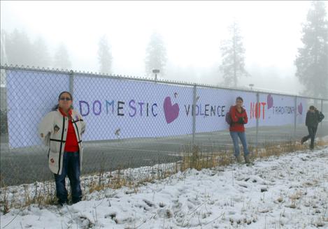 Evelyn Hernandez, left, Ashley Lozeau and Ida Couture stand by a banner constructed by Ashley and Ida. The message reads “domestic violence is not traditional.”