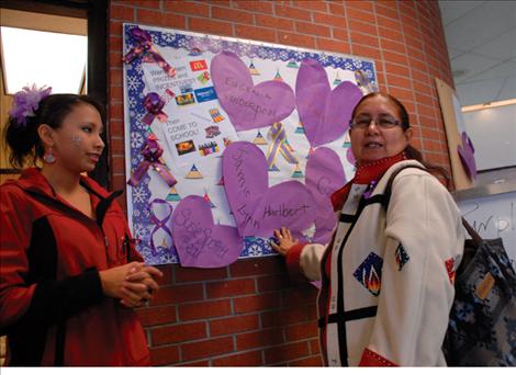 Ashley Lozeau and Evelyn Hernandez pose next to a bulletin board created in memory of women who lost their lives to domestic violence.