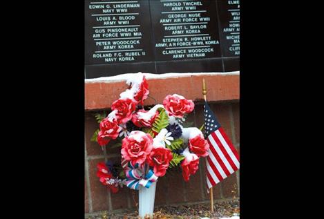 Snow covers frozen flowers beneath the names of the fallen.