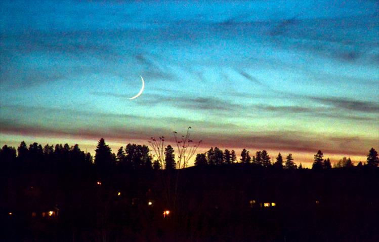 A slivery moon sets west of Polson Wednesday night as house lights begin to awaken.