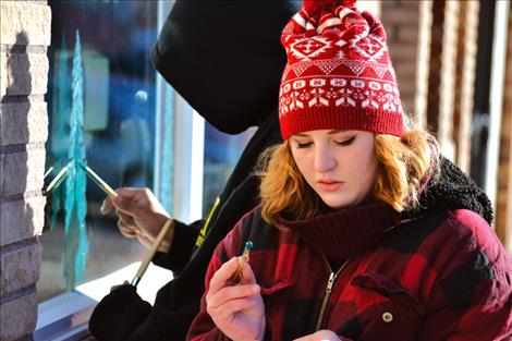 Ronan junior Andrea Stevens paints trees on Lucky Strike Lanes’ windows with senior Mario Yellow Owl