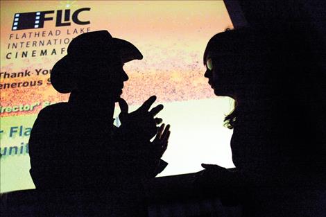 Two of last year’s festival goers stand silhouetted against a big screen as they discuss the films.