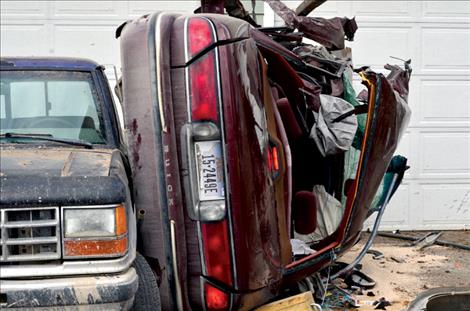 A maroon Buick stops on its side in a driveway after crashing into a city truck. 