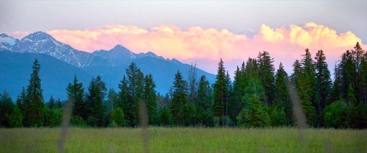 Sunset tints a bank of clouds behind the Mission Mountains with rose hues.