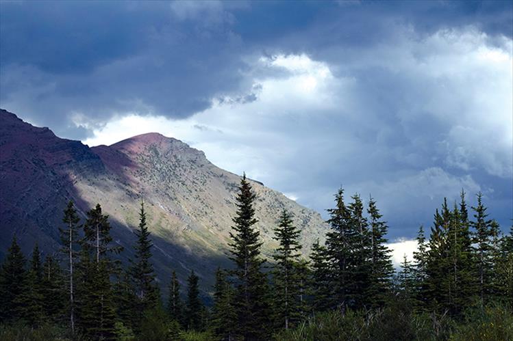 A break in the clouds allows the sun to illuminate a Glacier Lake mountain top.