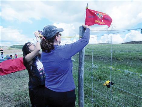 CSKT Tribal Council Member Shelly Fyant and Two Eagle River School student Naomi Stevens put their flag on a fence near pipeline contruction along with several other flags on the west side of the Missouri River.