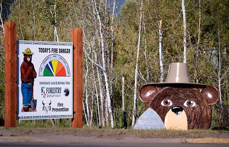 Two Smokey Bears, one of hay and one advising about daily fire danger, wear their signature hats as they look out on passersby.