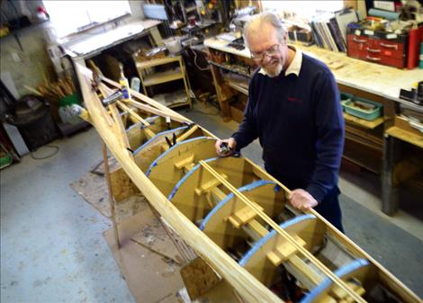 Gary Teggeman staples narrow cedar strips onto a strongback frame, above. Top right, he glances at the blueprint for his vessel created by Guillamot Kayaks. Top left, he dampens a wave inset created from contrasting cedar.