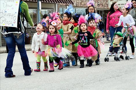 a line of children hold onto a rope to stay together and wave to the crowd.