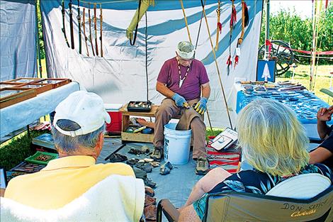 A small crowd gathers to watch  Don Safford as he works on chiseling down flint to make an arrowhead.