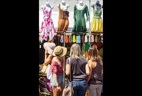 : Four lady shoppers consider four ladies’ dresses at a vendor’s display.
