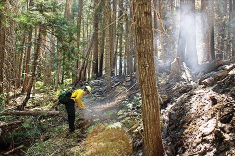 Information Officer Jacob Welsh stops to stirs some coals along the hand line, an area the fire fighters clear cut to help prevent the fire’s spreading. 