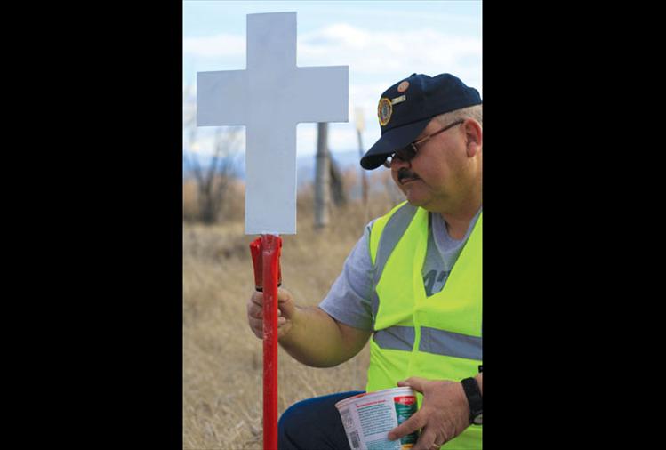 J.C. Courville, a local veteran and member of the Mission Valley Honor Guard repaints a white cross that marks the site of a fatal accident. He said that while the idea has been taken up by other states around the nation, veterans in Montana were the first to build, plant and maintain these markers. The crosses serve to remember the departed and remind motorists to drive carefully.