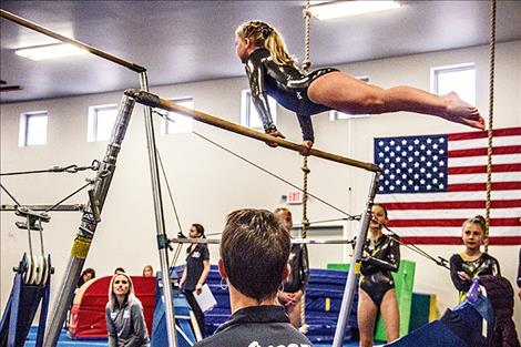 Felicity Mihara competes on the bars as teammates Olivia Valentine and Cyela Nault, and Coach Alysha Valentine watch. Felicity took the gold on bars.