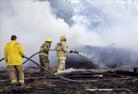 Charlo-Moiese and Ronan firefighters shoot water onto an abandoned mobile home last week. A grass fire destroyed the trailer, but firefighters controlled the fire before it spread.