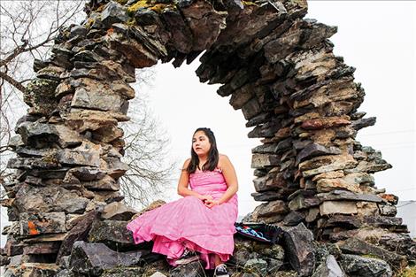 Carlee Rosbach sits on a stone arch between the Mission church and the Longhouse in St. Ignatius.