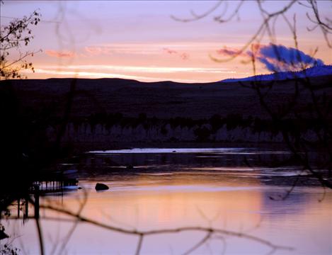 Sunset over the Flathead River paints the sky with streaks of pink and orange. The peaceful scene belies turmoil over a water rights compact making its way through the state legislature.