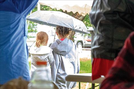 Children watch the rain from under an umbrella.