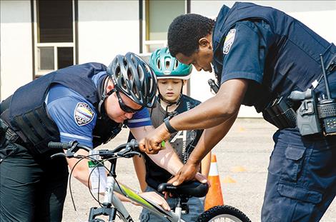 Polson Police Officers Keith Deetz and Hazeez Fafiu lower the seat on a bike so a child can ride it through their safety course during the Back to School  Wellness Fair on Saturday. 